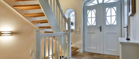 A staircase with wooden steps and white railings, a white door with arched windows, and a stone-tiled floor.