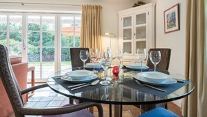 A dining area with a glass table set for four, surrounded by wicker chairs, with a view of greenery outside. - Luv Hüs - Luv Hüs - Geräumige Haushälfte in Keitum (Sylt-Ost)