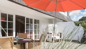 A patio with wicker furniture, a table, and an umbrella. - Luv Hüs - Luv Hüs - Geräumige Haushälfte in Keitum (Sylt-Ost)