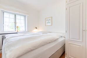 Une chambre à coucher avec un lit double, une fenêtre avec des rideaux, une lampe de chevet et une porte.