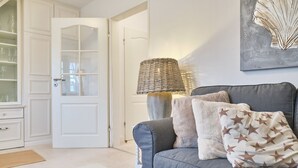 A living room with a grey sofa, a glass coffee table, a wicker lamp, and a door with glass panels.
