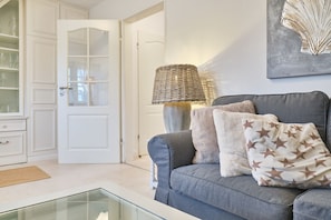 A living room with a grey sofa, a glass coffee table, a wicker lamp, and a door with glass panels.