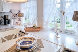 A bright kitchen with white cabinets, a coffee maker, a wicker basket with a rose, and a sailboat model.