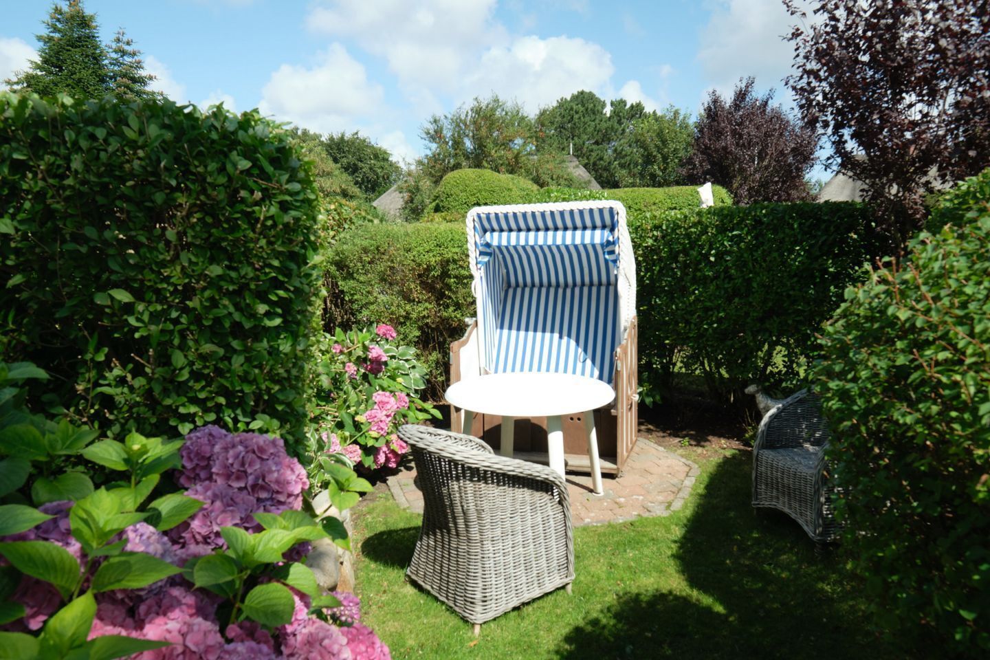 A garden with a wicker chair, a striped chair, and a small table.