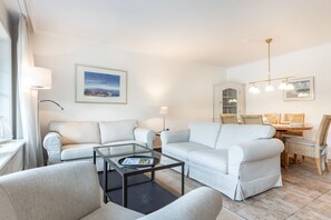 En moderne stue med to sofaer, et sofabord i glas og et spiseområde med bord og stole.