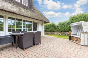 En terrasse med et bord og stole, et stråtækt tag og en stenvæg.