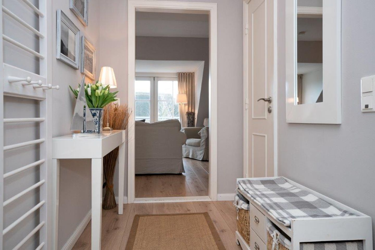 A narrow hallway leading to a living area with a sofa, a lamp, and a small table with a plant.