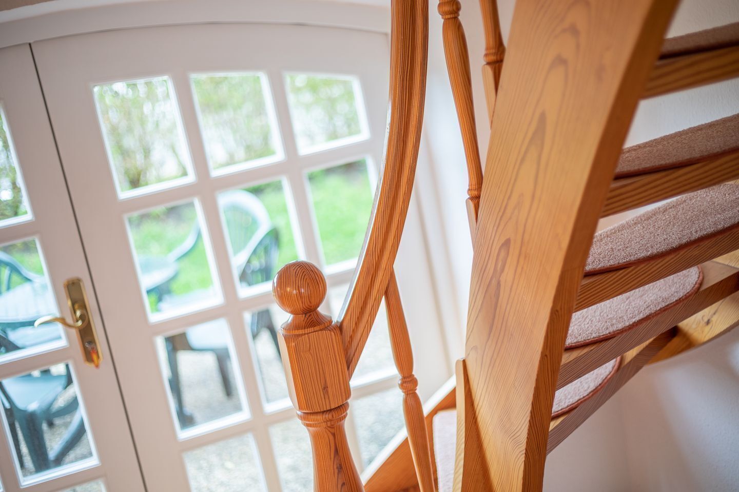 Una escalera de madera con barandilla y una puerta con paneles de vidrio.
