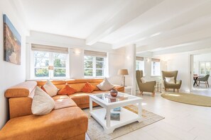 Un salón espacioso con un sofá naranja grande, una mesa de centro blanca y un sillón verde.