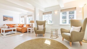 Ein modernes Wohnzimmer mit einem beigefarbenen Sofa, zwei Sesseln, einem Couchtisch und einem Teppich.