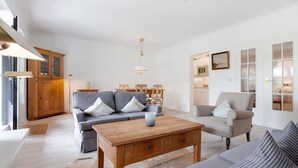 A modern living room with a sofa, armchairs, a wooden coffee table, and a dining area with a table and chairs. - Weber EG - Weber EG - Wohnen Unter Reet im Kapitänsdorf Keitum (Sylt-Ost)