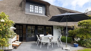 A thatched-roof house with a patio, white outdoor furniture, and a black umbrella. - Weber EG - Weber EG - Wohnen Unter Reet im Kapitänsdorf Keitum (Sylt-Ost)