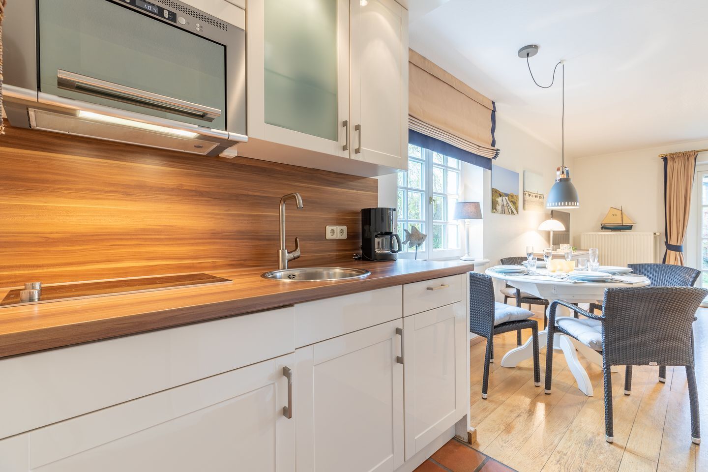A modern kitchen with a wooden countertop, stainless steel appliances, and a dining area with wicker chairs and a table.