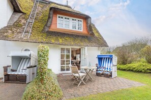 A house with a thatched roof, a wooden deck, a dining area with outdoor furniture, and a small garden.