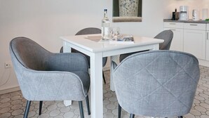Comedor con una mesa blanca, cuatro sillas grises tapizadas, una botella y un vaso sobre la mesa.
