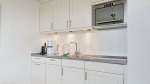 Una cocina moderna con armarios blancos, horno de acero inoxidable y cafetera.