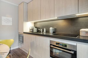 Una cocina moderna con armarios de madera, encimera negra, horno empotrado y cafetera.