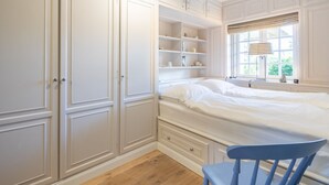 Une chambre à coucher comprenant un lit, des étagères intégrées, une fenêtre avec vue et un fauteuil.