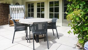 Une terrasse avec une table ronde et des chaises, un toit de chaume et une grande fenêtre.