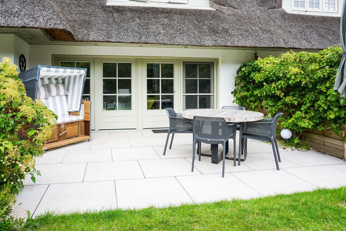 A patio with a round table and chairs, a thatched roof, and a white door.