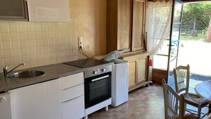 Kompakti keittiö, jossa on pesuallas, uuni ja kaapit, ruokailutila tuoleineen sekä näkymä ikkunasta.