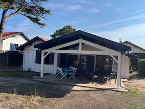 A covered outdoor patio with a table and chairs, adjacent to a house with a red roof. - Chalet 'Quartier Des Pêcheurs Réf 35' with Private Garden (Lège-Cap-Ferret)