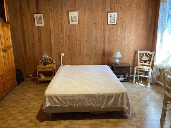 A bedroom with a bed, wooden walls, a nightstand, a chair, and a lamp.