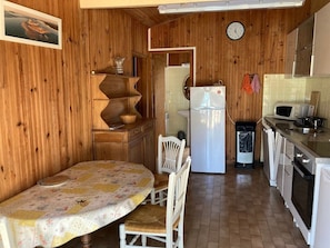 A wooden interior with a dining table, chairs, a refrigerator, a microwave, and a sink. - Chalet 'Quartier Des Pêcheurs Réf 35' with Private Garden (Lège-Cap-Ferret)
