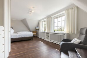 A bedroom with a bed, a chair, a desk, a radiator, and a window with curtains.