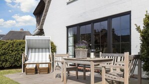 An outdoor seating area with a table and chairs, a wicker basket with flowers, and a large window. - Süderwind 2 - Süderwind 2 - Komplett Renoviertes Mittelhausteil Über 3 Ebenen (Sylt-Ost)