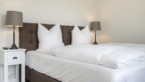 A neatly made bed with white linens and a brown headboard. There are two bedside tables with lamps on either side of the bed. - Süderwind 2 - Süderwind 2 - Komplett Renoviertes Mittelhausteil Über 3 Ebenen (Sylt-Ost)