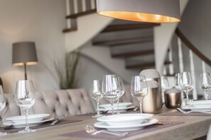 Una mesa de comedor dispuesta con copas de vino, platos y cubiertos, con una lámpara moderna sobre ella.