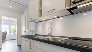 A modern kitchen with white cabinetry, a black countertop, and stainless steel appliances. - Lüüvwai II - In Einer Reetgedeckten Wohnanlage in Südlage Nahe dem Benen-diken-hotel (Sylt-Ost)