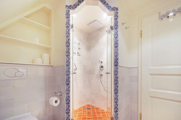 Un baño con azulejos blancos, ducha e inodoro.
