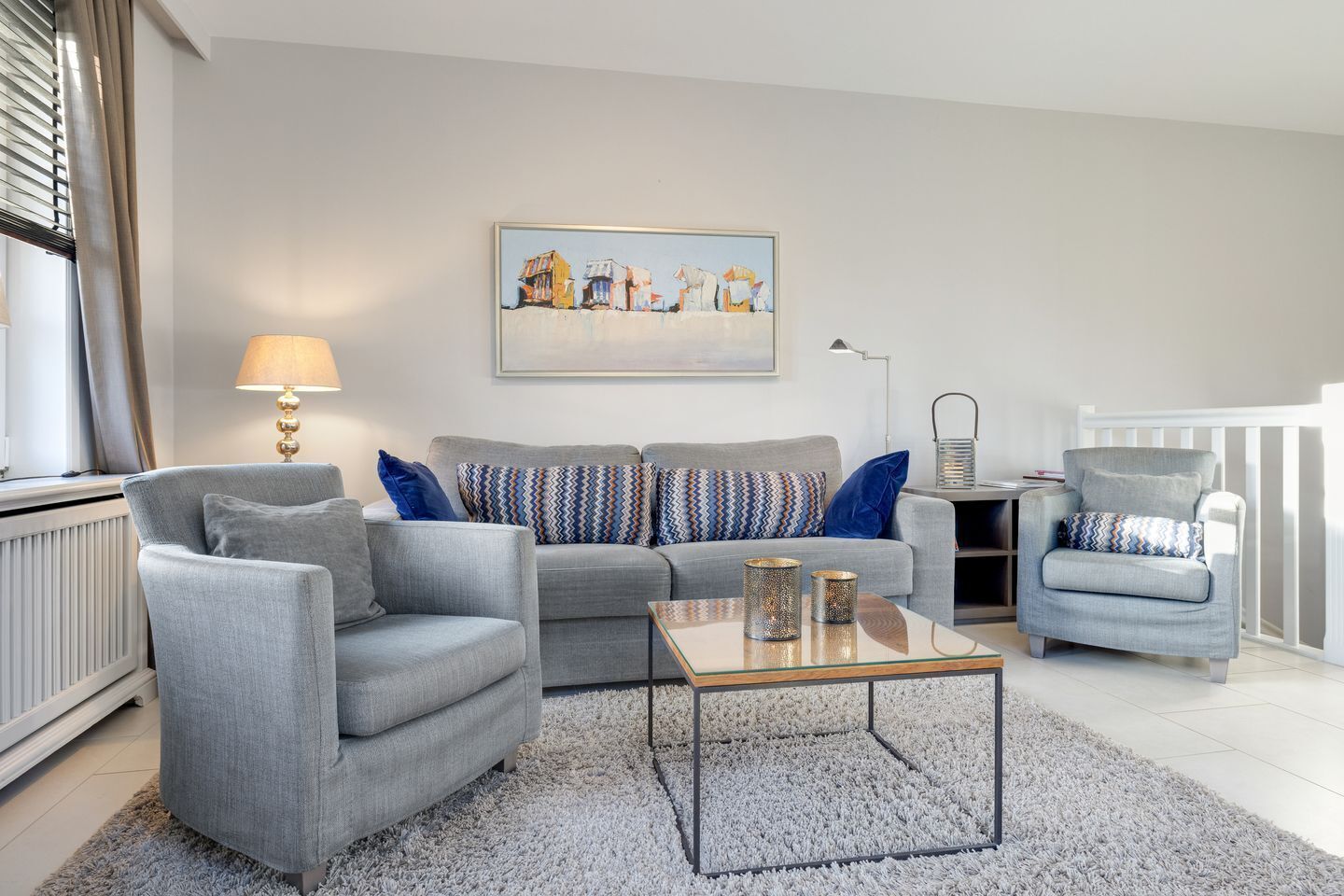 A modern living room with a grey sofa, armchairs, a glass coffee table, and a painting on the wall.