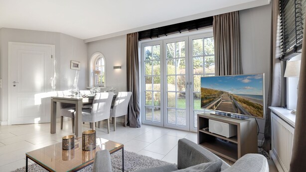 A modern living room with a dining area, large windows, and a flat-screen TV. - Litz Hüs - Litz Hüs - Reetgedeckte Wohnung Liegt Idyllisch im Süden von Keitum (Sylt / OT Keitum)