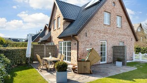 A two-story brick house with a sloped roof, a patio with a table and chairs, and a small garden area. - Gode Tiet - Gode Tiet - Schöner Neubau im Herzen von Westerland (Sylt)