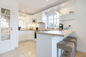 Een moderne keuken met witte kasten, een centraal eiland, barkrukken en een raam dat voor natuurlijk licht zorgt.