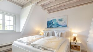 A bedroom with a large bed, a painting of a wave, and a window. - Kleine Heimat - 2-raum-appartement im OG, ca. 50m² Nutzfläche (Sylt)