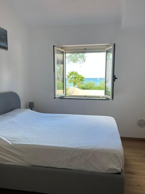 A bedroom with a bed, a window with a view of the sea, and a lamp. - Villa 'Edith' with Sea View, Shared Pool, and Air Conditioning (Parghelia)