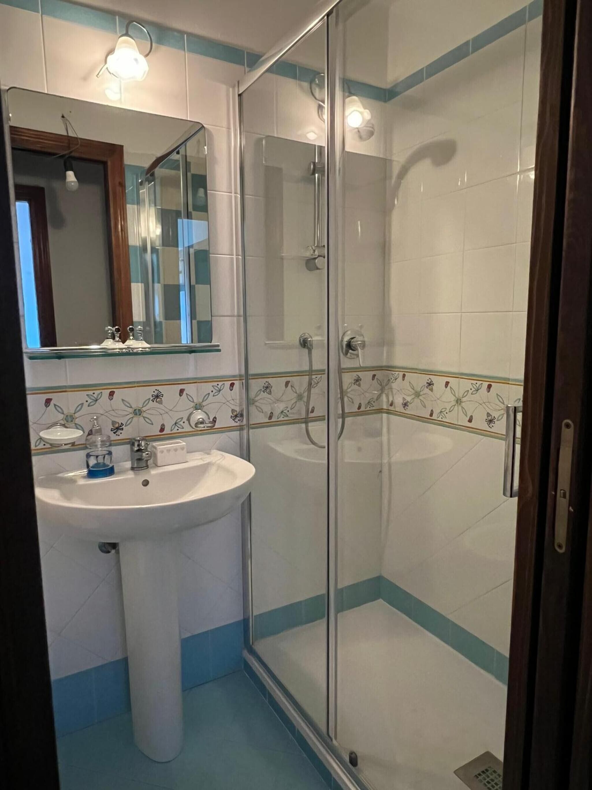 Une salle de bain avec une douche à parois de verre, un lavabo avec un miroir au-dessus et des carreaux décoratifs.