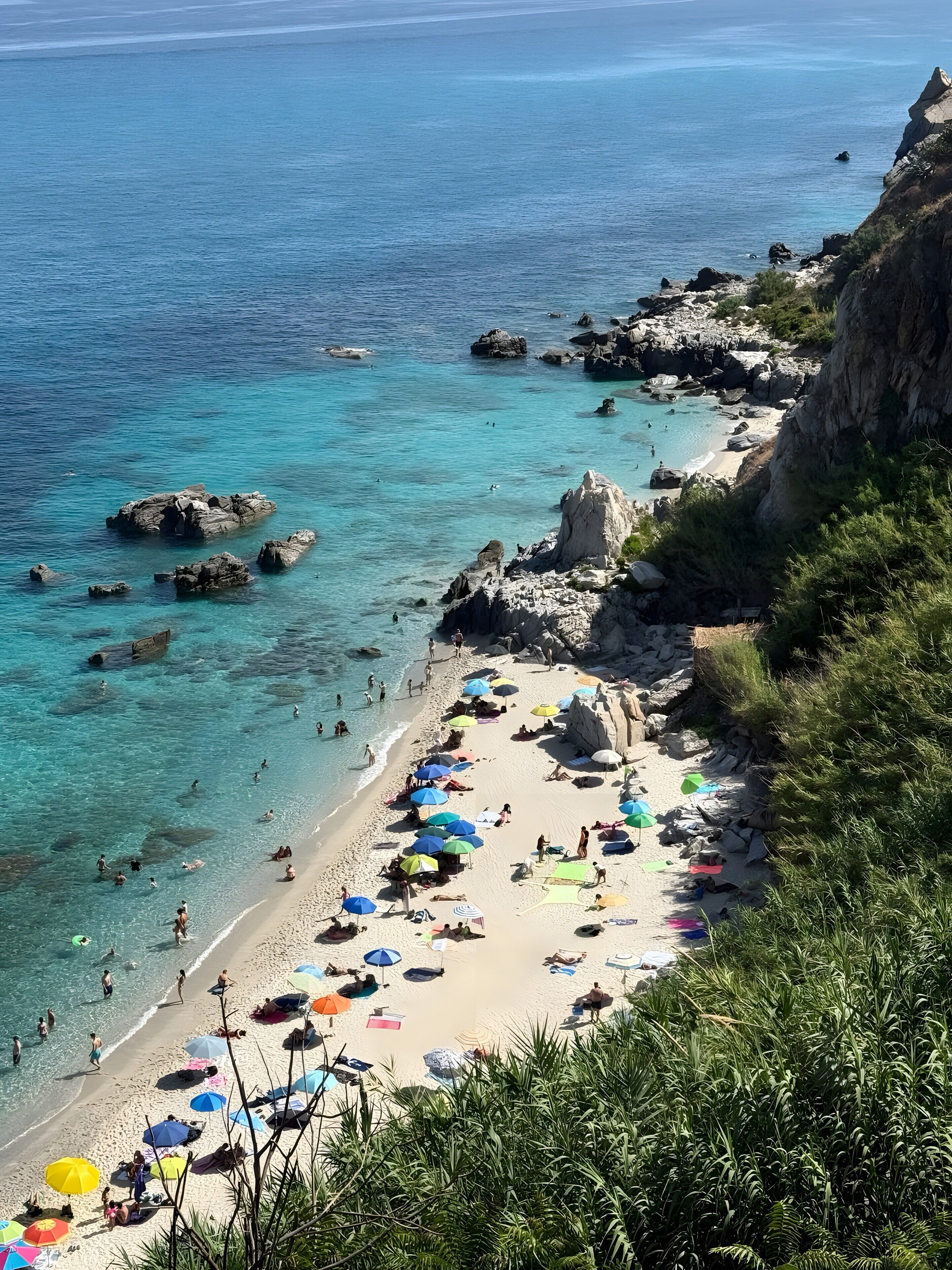 Een strand met helder turquoise water, rotsachtige uitstulpingen en mensen die zonnebaden.