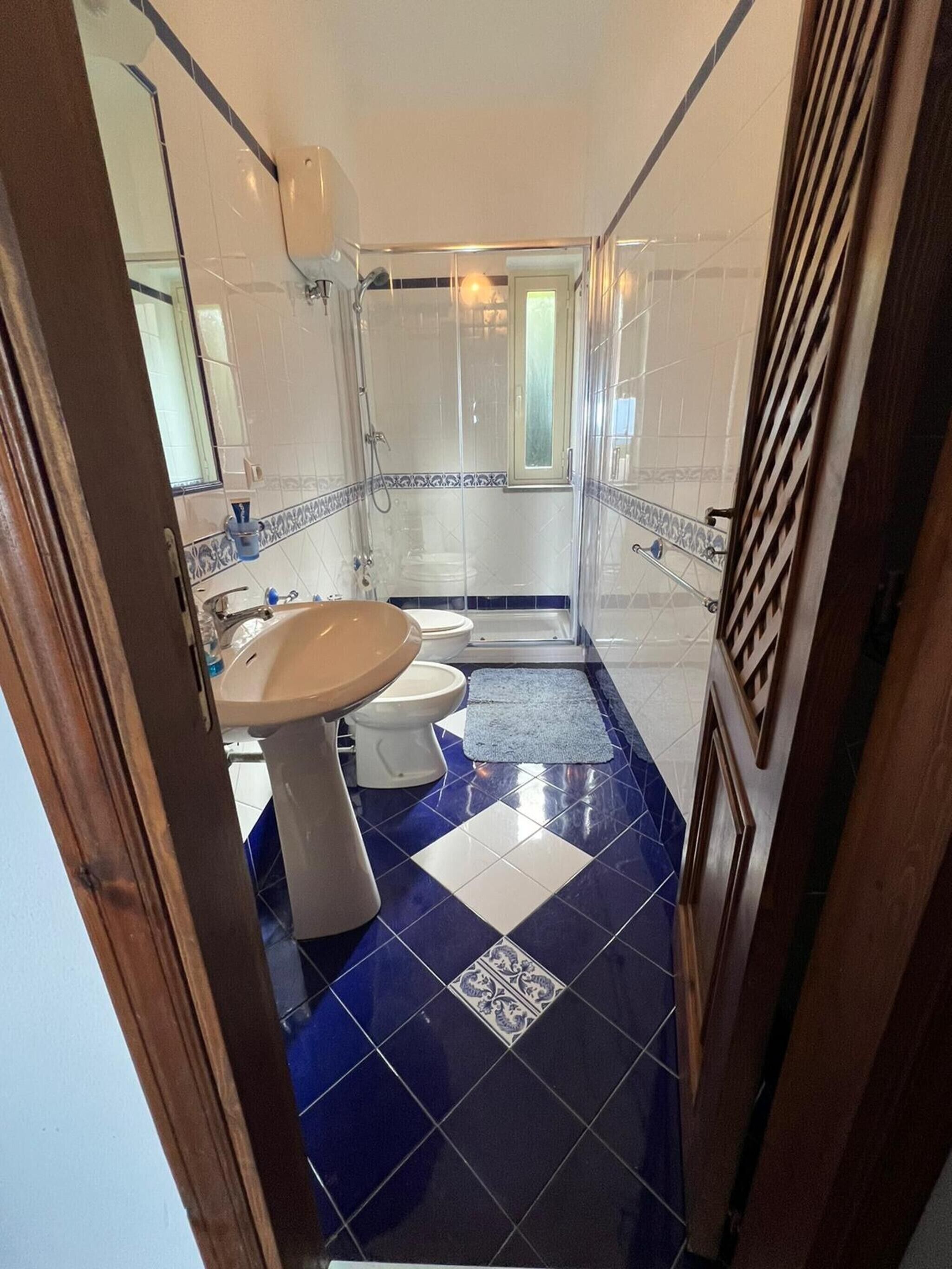 Ein Badezimmer mit Waschbecken, Toilette und Duschbereich, mit blauen und weißen Fliesen sowie einem strukturierten Fliesenmuster.
