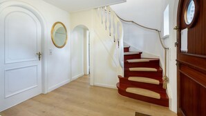 Un escalier avec des marches en bois et une main courante en corde, menant à un palier avec une porte blanche et un miroir.