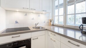 Una cocina moderna con muebles blancos, estufa integrada, un lavamanos y una ventana con vista a árboles.