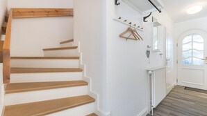 Una escalera con escalones de madera, una pared blanca, un perchero y un radiador.