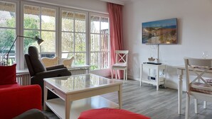 Una sala moderna con una mesa de centro de vidrio, un sofá rojo, una mesa de comedor blanca y un cuadro en la pared.