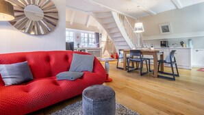 Ein modernes Wohnzimmer mit einem roten Sofa, einem Essbereich mit Holztisch und Stühlen sowie einer Treppe zu einer oberen Ebene.