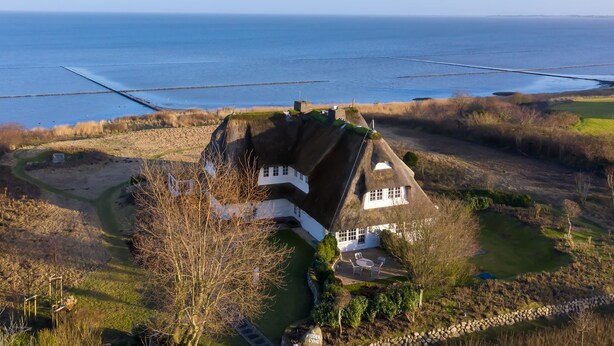 Ein Haus mit Strohdach, umgeben von einem angelegten Garten und Blick auf das Meer.