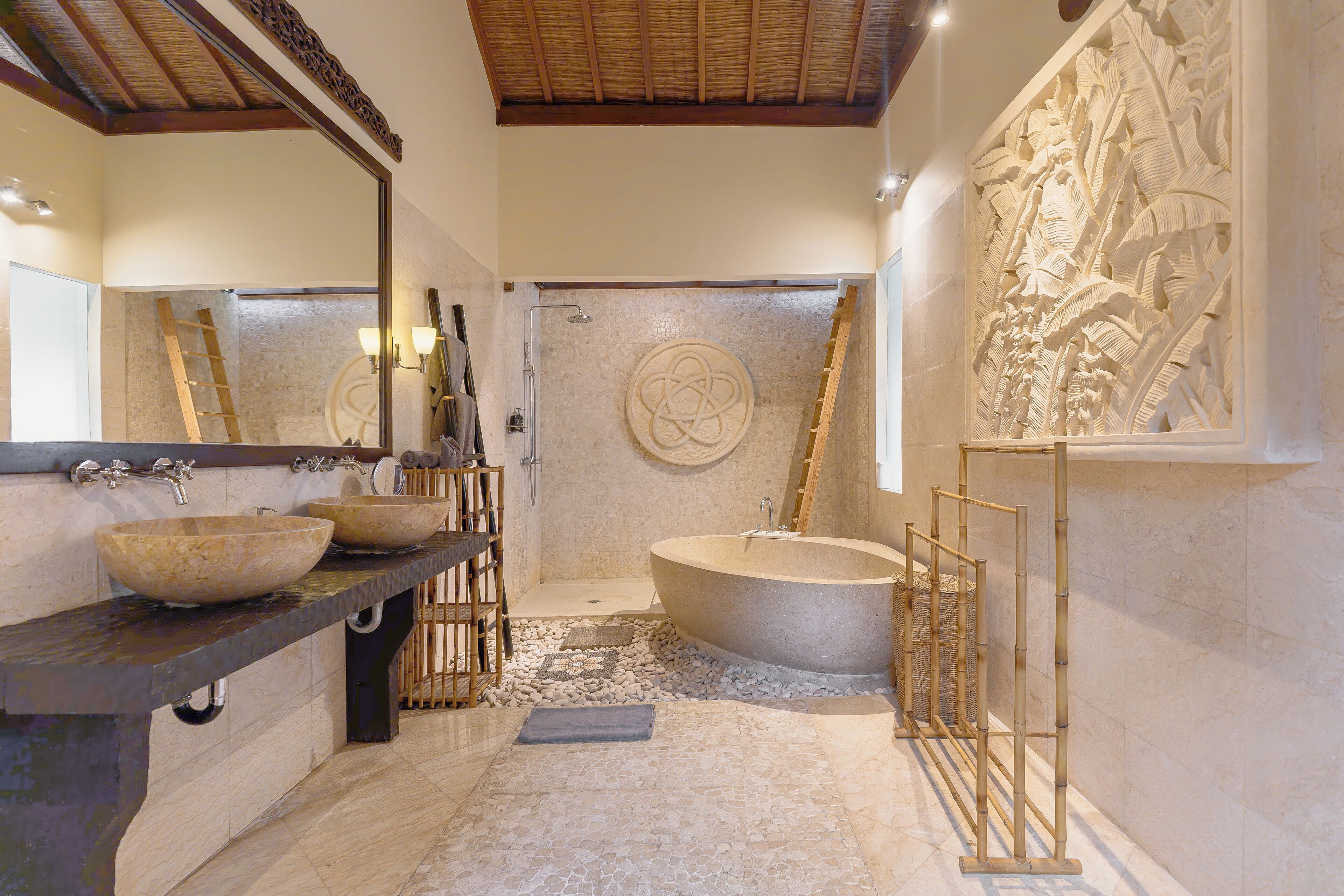 A modern bathroom with a large freestanding bathtub, a double sink with a large bowl, and a decorative wall carving.